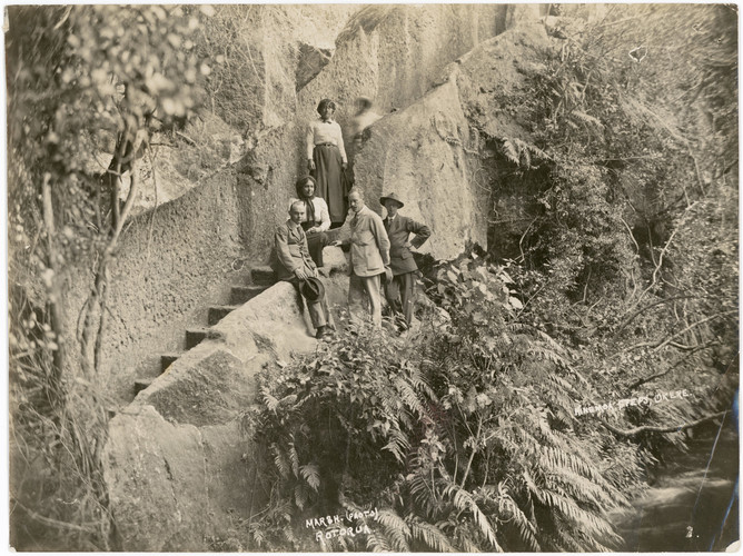 A black and white photo of five people in Edwardian dress standing on steps carved into rock and surrounded by vegetation.