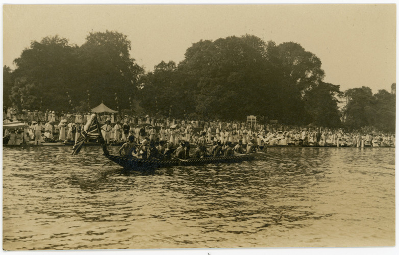 A waka on the river at Henley with a large crowd watching from the bank.