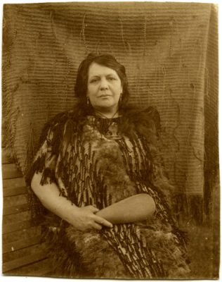 A black and white photo of Makareti as an older woman seated in front of a kaitaka garment.